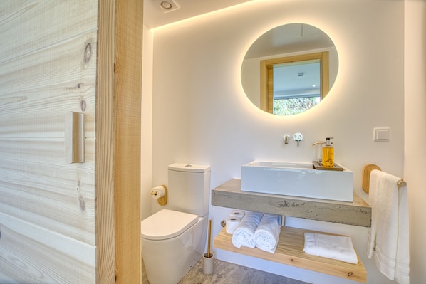 A modern bathroom with a wooden vanity, a round mirror, and a toilet. - Socalco Nature Calheta (Calheta)