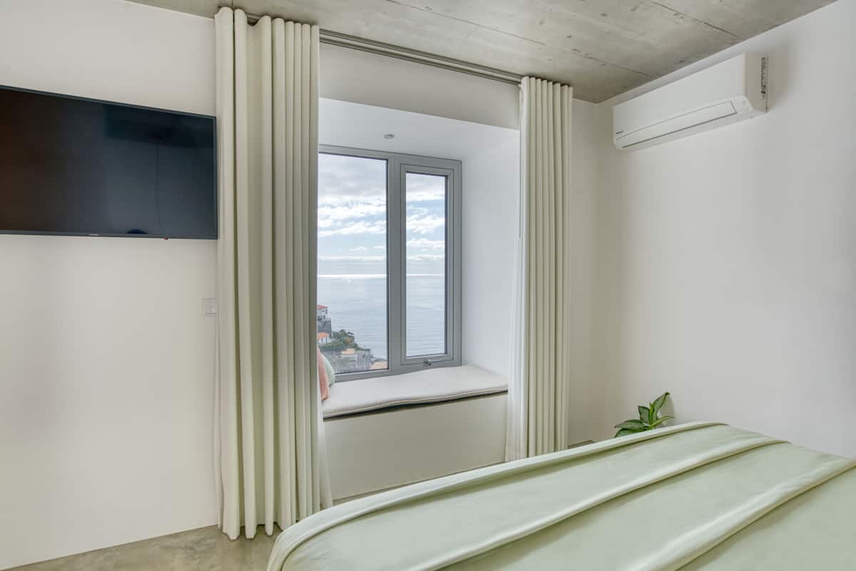 Quarto com uma janela grande, uma cama, uma TV e aparelho de ar condicionado.