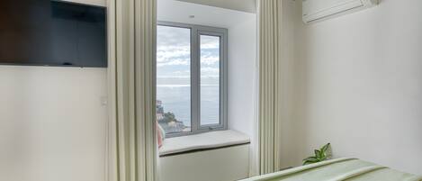 A bedroom with a large window, a bed, a TV, and an air conditioning unit.