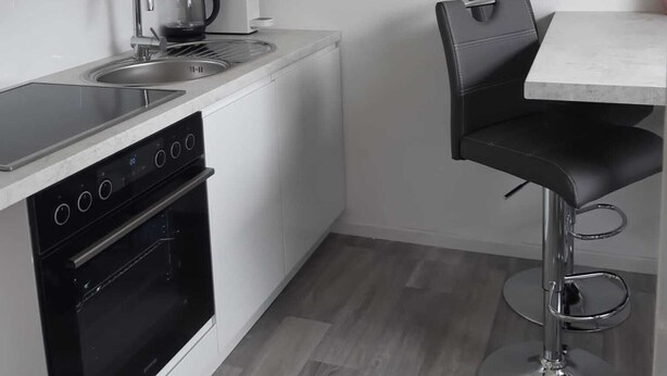 A compact kitchen with a built-in oven, a kettle, and a modern faucet. - D&B staycation Ferienpark (Niedenstein)