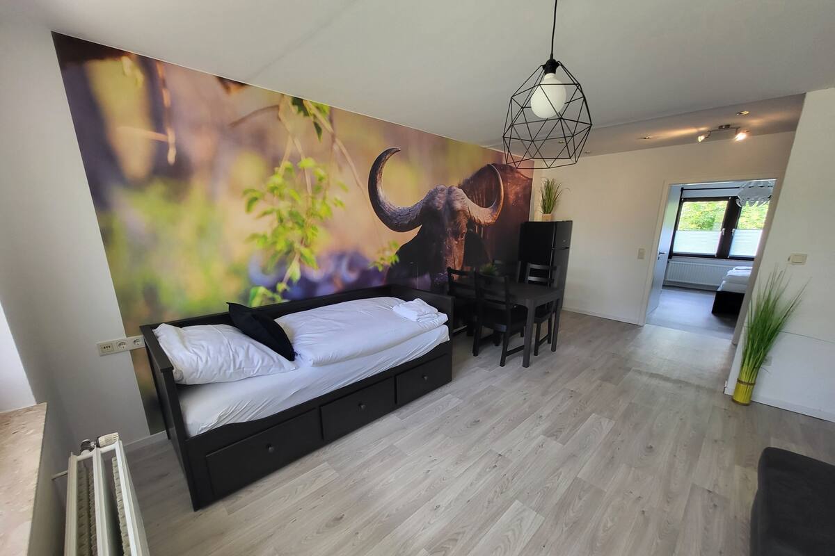 A modern living room with a bed, a dining area, and a large mural on the wall.
