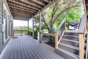 A covered wooden deck with a metal railing and stairs leading to a covered area.