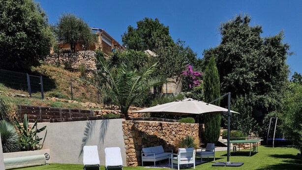 A swimming pool with lounge chairs and a table, surrounded by greenery and a stone wall. - Quiet modern villa with swimming pool (Le Tignet)