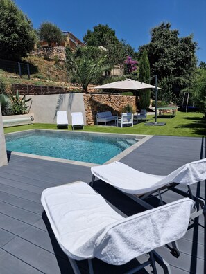 A swimming pool with lounge chairs and a table, surrounded by greenery and a stone wall.