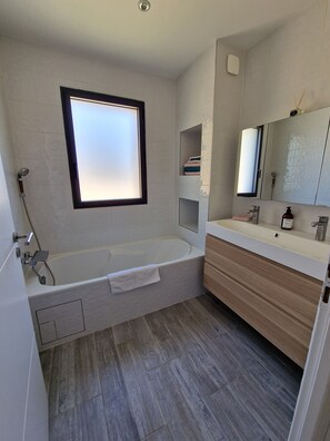 Een bad/douchecombinatie, een haardroger, handdoeken, toiletpapier