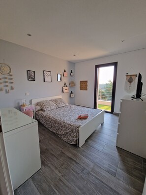A bedroom with a bed, a desk, a dresser, and a wardrobe. There are wall decorations and a window with a view.