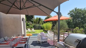 An outdoor patio with a grill, dining tables, and umbrellas. - Quiet modern villa with swimming pool (Le Tignet)