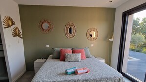 A modern bedroom with a large bed, decorative wall mirrors, and a view of the outdoors through a large window. - Quiet modern villa with swimming pool (Le Tignet)