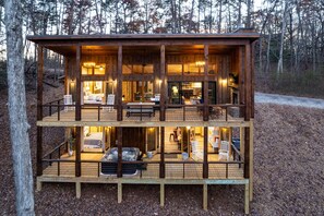 Une cabane en bois à deux étages, dotée d’une terrasse, d’un jacuzzi et d’un coin cuisine.