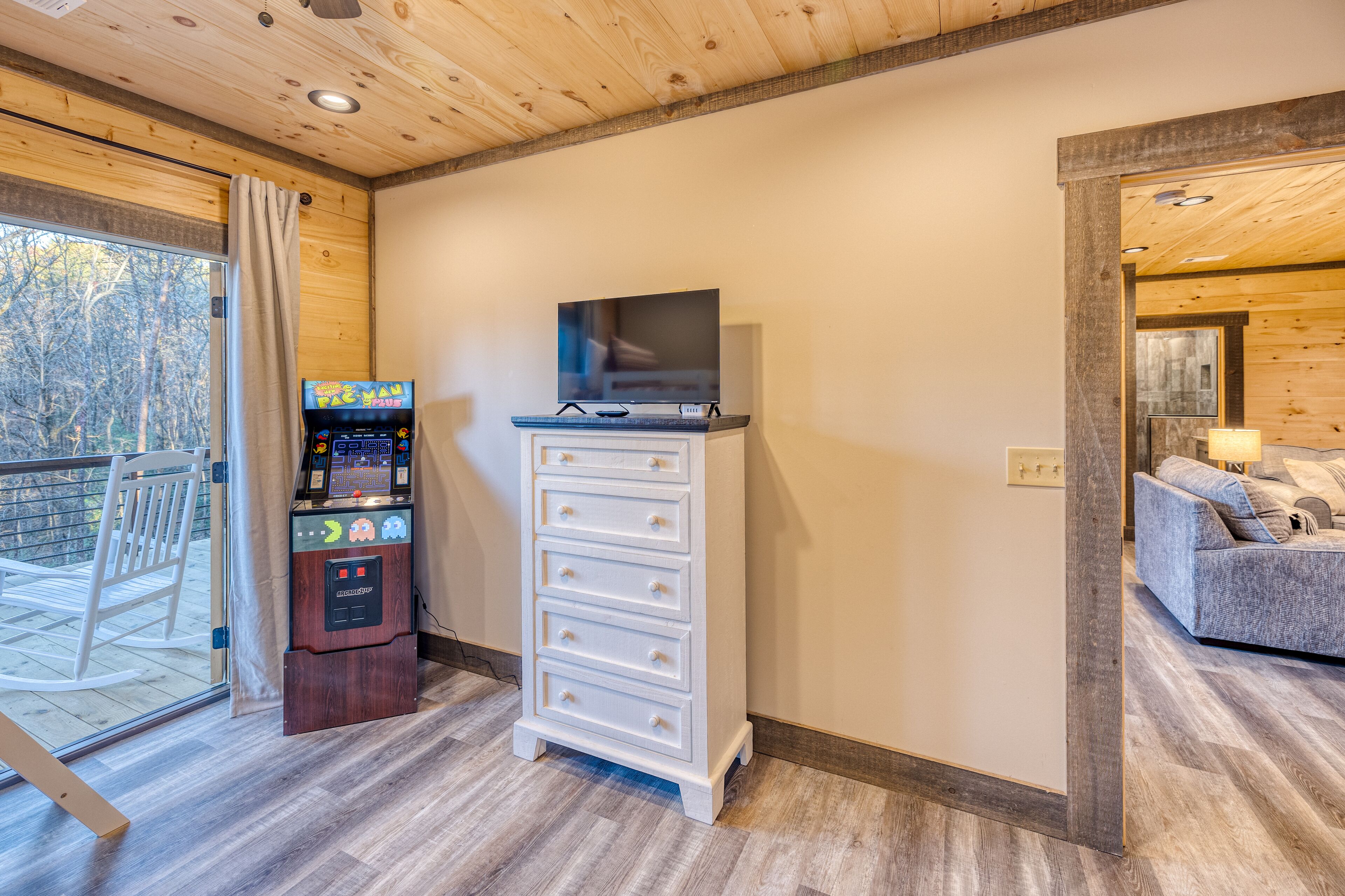 A room with a wooden ceiling, a TV on a dresser, a game console, and a sofa.