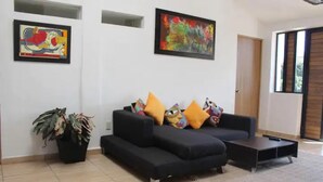 A modern living room with a black sectional sofa, colorful cushions, a coffee table, and two abstract paintings on the walls. - Beautiful Guest House with Pool, Jacuzzi & Garden (Lomas de Cocoyoc)