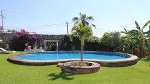 A circular swimming pool surrounded by a well-maintained lawn, with a palm tree in the center and a stone wall in the background. - Beautiful Guest House with Pool, Jacuzzi & Garden (Lomas de Cocoyoc)
