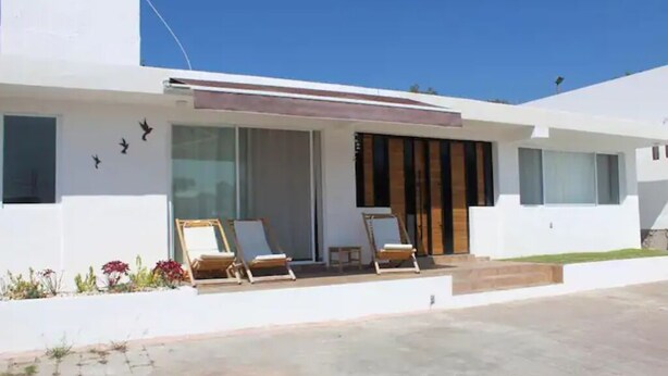 A modern house with a large glass door, two wooden chairs outside, and a clear blue sky. - Beautiful Guest House with Pool, Jacuzzi & Garden (Lomas de Cocoyoc)