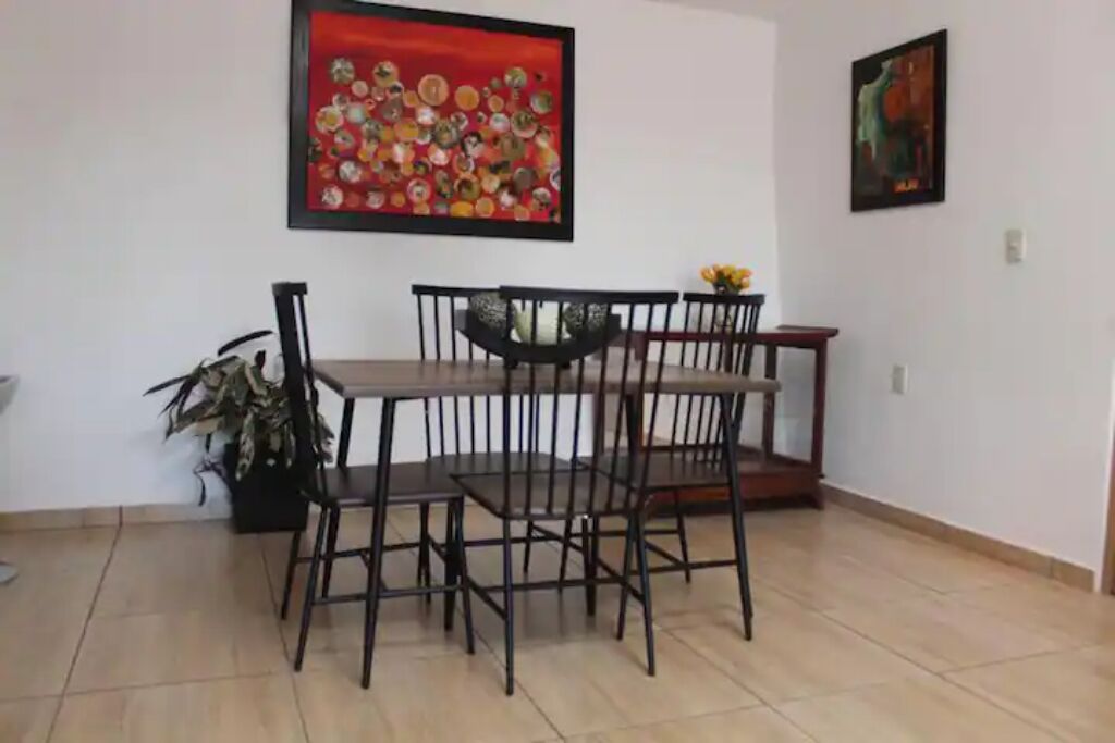 Een eethoek met een tafel en stoelen, een plant in pot en twee kunstwerken in lijsten aan de wanden.