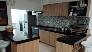 A modern kitchen with wooden cabinets, black countertops, and a tiled backsplash. - Beautiful Guest House with Pool, Jacuzzi & Garden (Lomas de Cocoyoc)