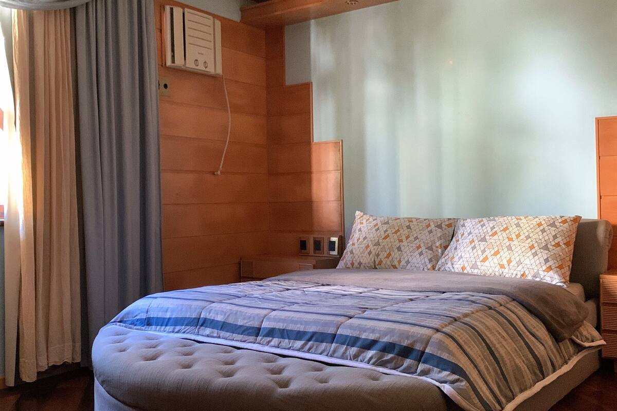 Un dormitorio con cama, cortinas, una ventana y cabecera de madera.