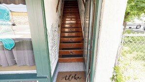 Una escalera de madera que lleva a una puerta con un felpudo que dice 'Aloha'.