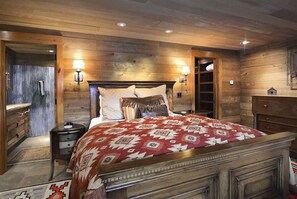 Une chambre à coucher avec une tête de lit en bois, deux lampes de chevet, un lit recouvert d’une couvre-lit à motifs, une table de chevet et une commode.