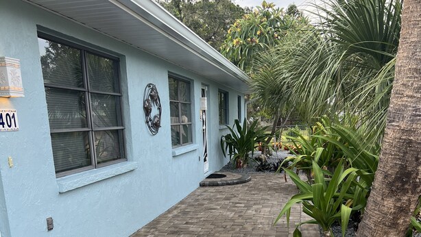 Un edificio azul claro con un sendero pavimentado, un cartel con el número '401' y plantas tropicales.