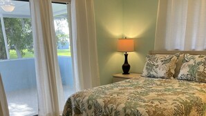 Un dormitorio con cama, mesita de noche, lámpara y vistas al exterior.
