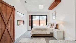 Une chambre à coucher avec un grand lit, une table de chevet, une porte en bois et une porte-fenêtre coulissante donnant sur l’extérieur.