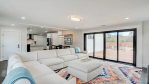 Un salon moderne avec un canapé d’angle, un tapis coloré et une grande porte-fenêtre coulissante donnant sur l’extérieur.