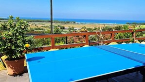 Une table de ping-pong bleue sur un balcon extérieur, avec vue sur la mer et la campagne.