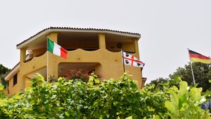 Un bâtiment orné de plusieurs drapeaux, dont le drapeau italien, un drapeau avec une croix et un emblème noir, et le drapeau allemand.