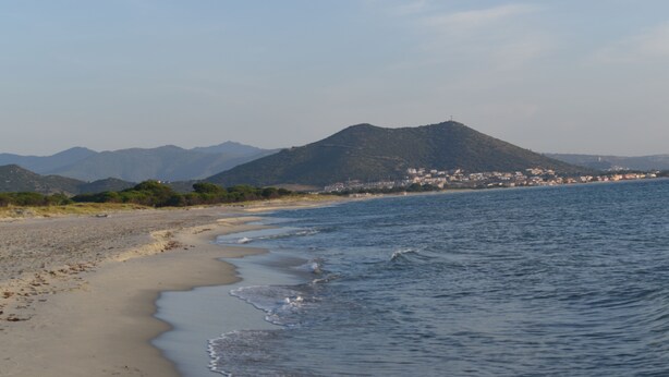 Une plage avec une montagne en arrière-plan et une ville de l’autre côté de l’eau.