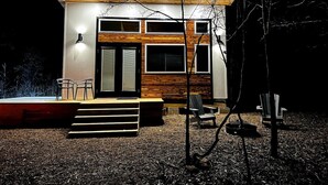 Una casa moderna con fachada de madera, un porche con escalones y una pequeña zona de estar al aire libre con sillas.