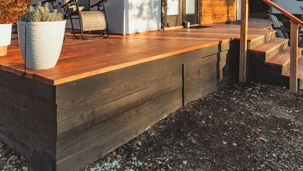 Una casa moderna con terraza de madera, puerta de cristal y mobiliario exterior.