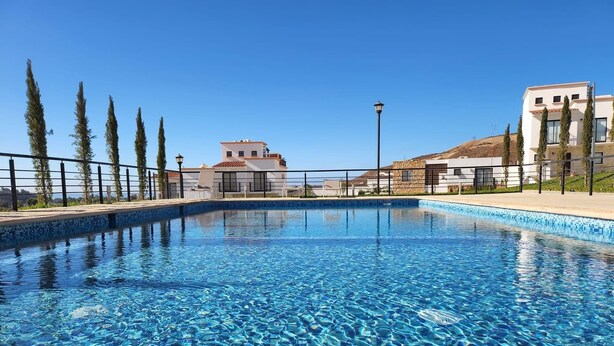 Ein klarer Swimmingpool mit einer gefliesten Kante, umgeben von einem Zaun und Bäumen.