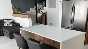 Eine moderne Küche mit einer weißen Kücheninsel, zwei Barhocker, einem Edelstahlkühlschrank und einer schwarzen Treppe.