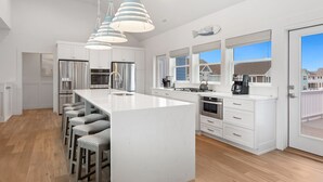 Een moderne keuken met witte kasten, roestvrijstalen apparatuur, een groot eiland met barkrukken en hanglampen.
