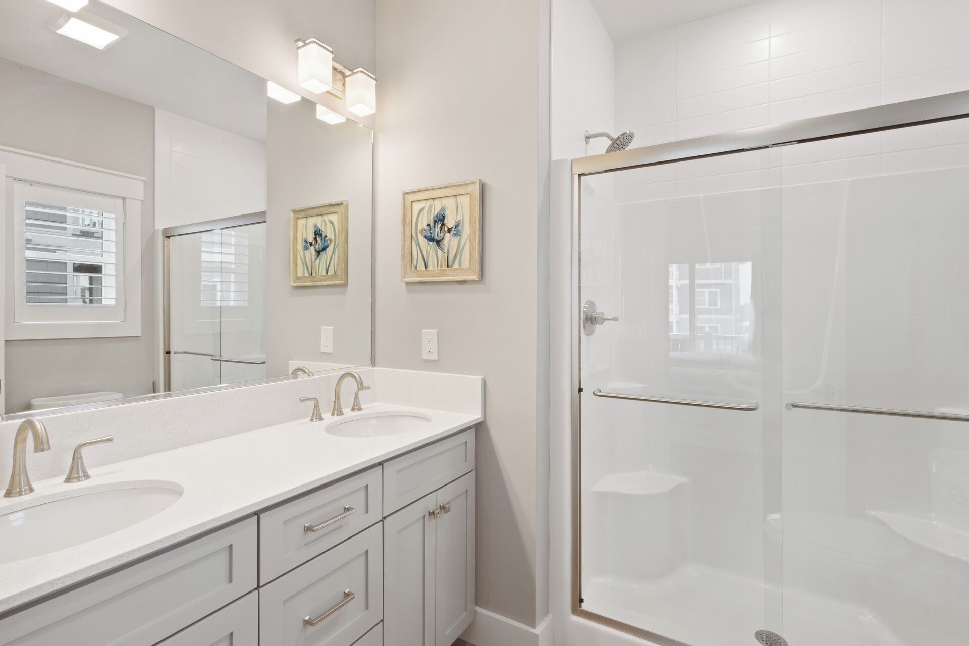 A modern bathroom with two sinks, a large mirror, and a glass-enclosed shower.
