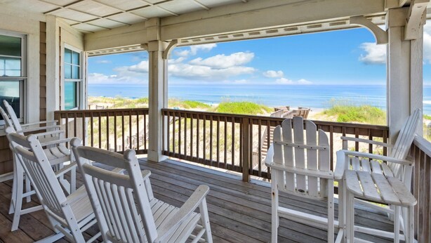 A covered deck with white Adirondack chairs, a wooden railing, and a view of the ocean. - Seaside Oasis *Oceanfront Luxury w/ PRIVATE Beach Walkway, Pool, Elevator, Media Rm, Pool Table... (Nags Head)