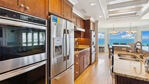 A modern kitchen with stainless steel appliances, wooden cabinets, and a view of the ocean. - Seaside Oasis *Oceanfront Luxury w/ PRIVATE Beach Walkway, Pool, Elevator, Media Rm, Pool Table... (Nags Head)