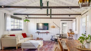 A spacious living room with a wooden dining table, a sofa, and a large TV.