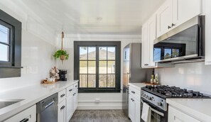 A modern kitchen with white cabinetry, a gas stove, and a window overlooking a backyard.