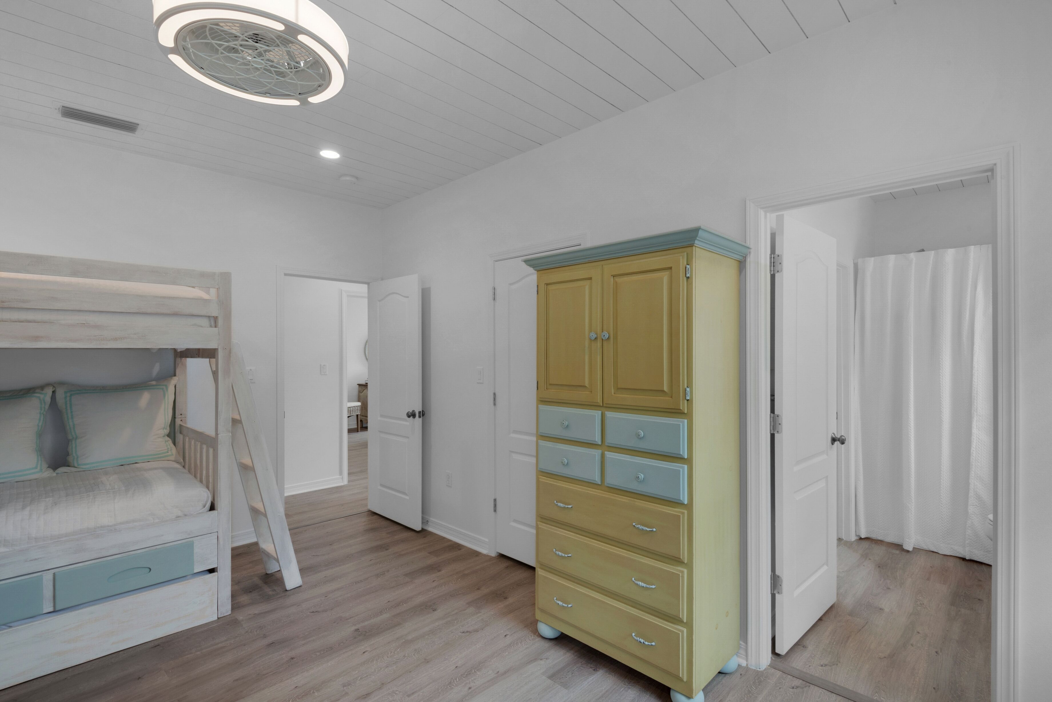A bedroom with a bunk bed, a dresser, and a door leading to another room.