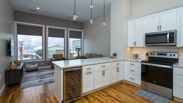 Une cuisine moderne avec des meubles blancs, un four à micro-ondes en acier inoxydable et un four traditionnel. Une grande fenêtre offre une vue sur la ville.