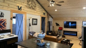 Un acogedor interior de cabaña con techo de madera, una chimenea, un televisor y un comedor con estufa.
