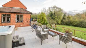 Een terras met tuinmeubilair, een hottub en een bakstenen huis op de achtergrond.