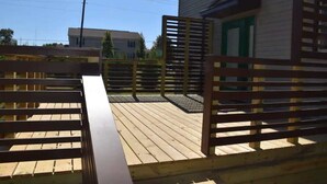 A wooden deck with a metal gate, a building with a green door, and a clear sky.