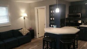 A compact living space with a kitchenette, a sofa, a coffee table, and a bar area with stools.