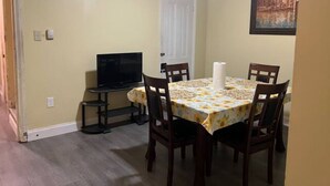 A dining area with a table set for six, a television on a stand, and a door in the background. - Rare 1 bedroom Gem (Wilmington)