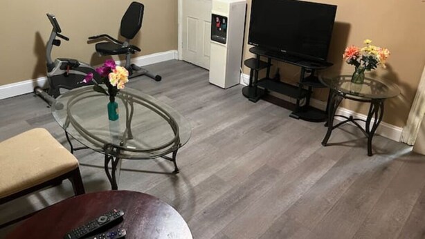 A living room with a TV, exercise equipment, a glass table, and a small table with flowers. - Rare 1 bedroom Gem (Wilmington)