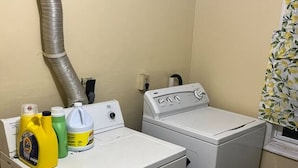 A laundry area with two white washing machines, a vent, and cleaning supplies on the counter. - Rare 1 bedroom Gem (Wilmington)