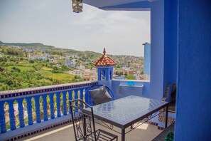 A balcony with a table and chair, overlooking a town with buildings and greenery. - Dar Jinane 2: Cosy and Stylish (Chefchaouen)