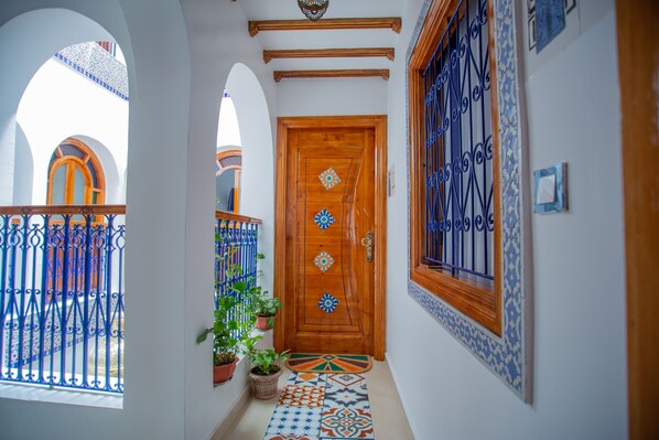 A hallway with a wooden door, potted plants, and a patterned floor. - Dar Jinane 2: Cosy and Stylish (Chefchaouen)